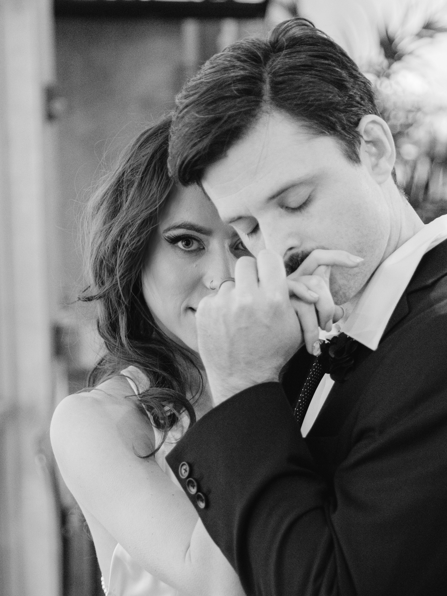 Close up black and white Virginia Beach engagement photography of a groom kissing bride's hand and her looking strait into the camera