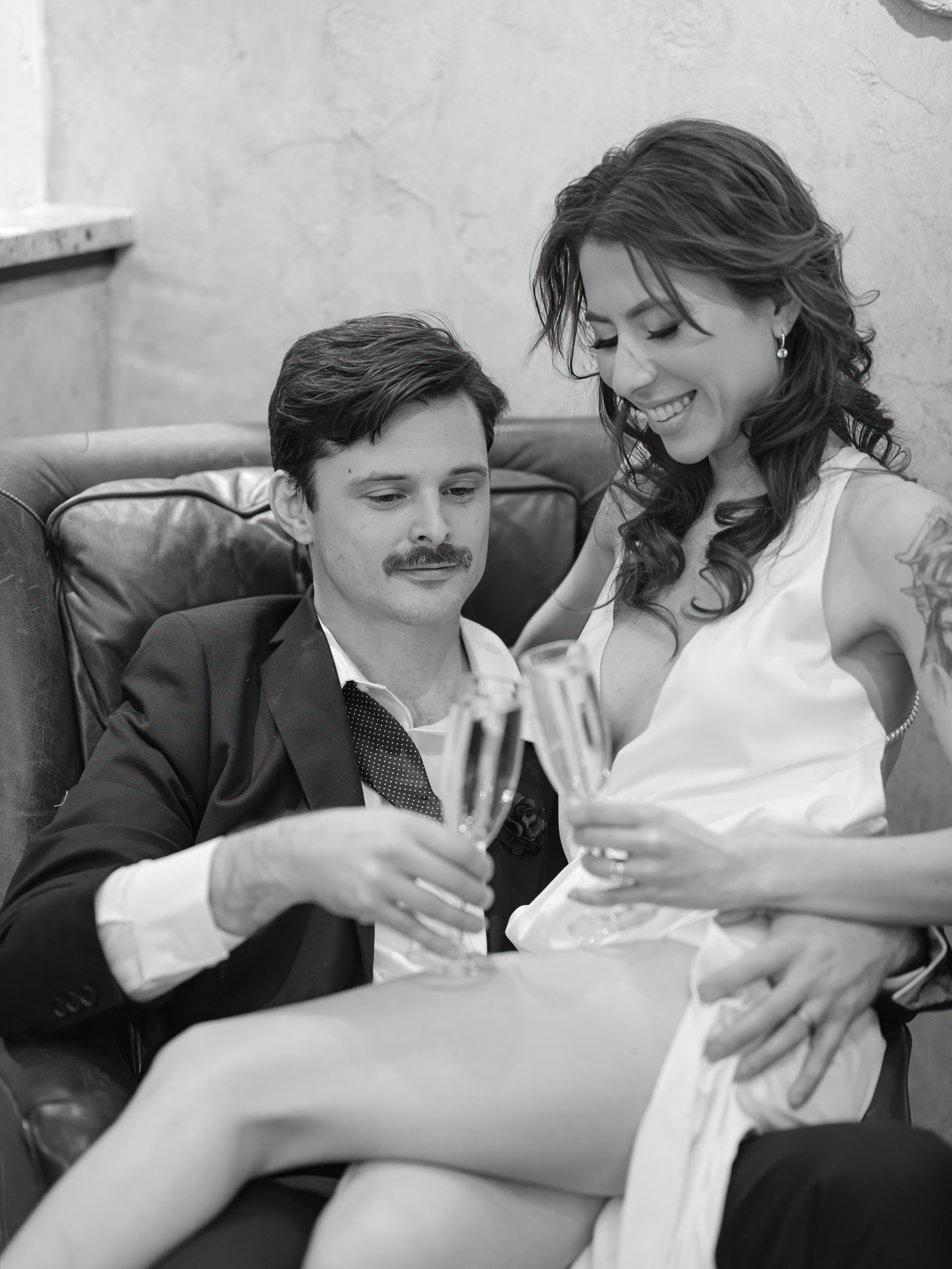 Black and white Virginia Beach engagement photography of a bride and groom clink glasses of champagne and laugh