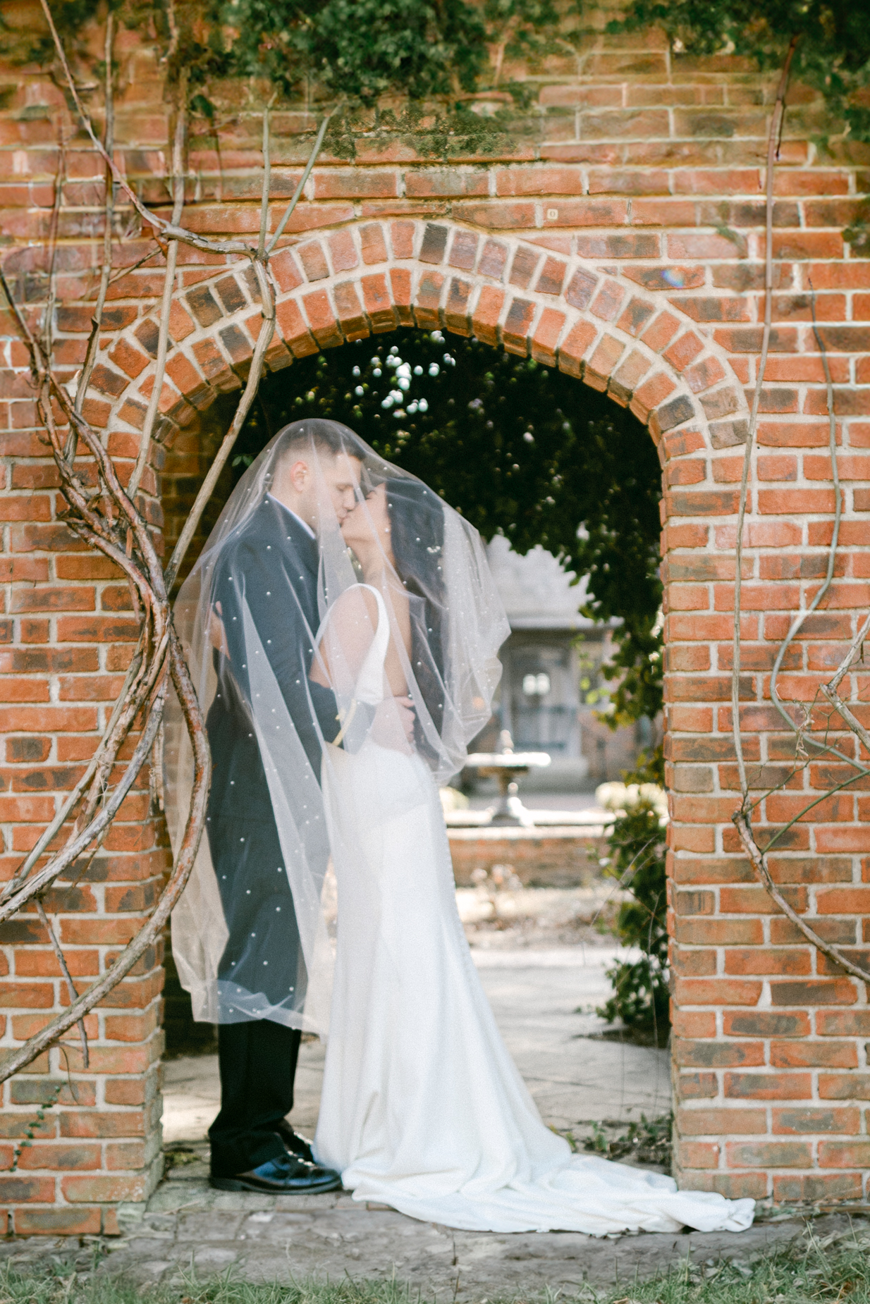 Hermitage Museum and Gardens  wedding photography of a bride and groom standing under a brick arch covered with vines and kissing