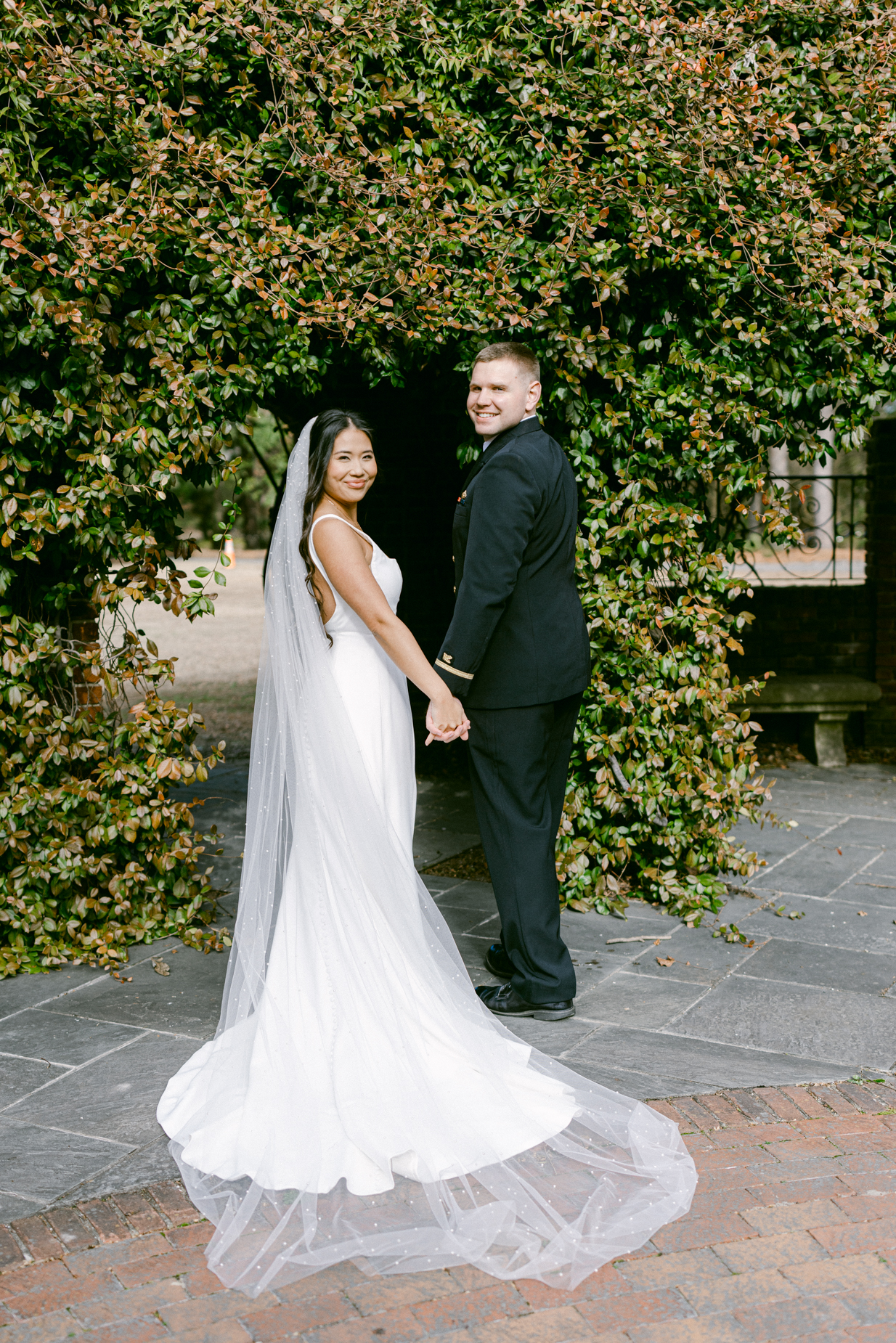 Hermitage Museum and Gardens  wedding photography of a bride and groom standing in front of pergola, holding hands and looking back, taken by Virginia Beach wedding photographers Glenn and Nadya