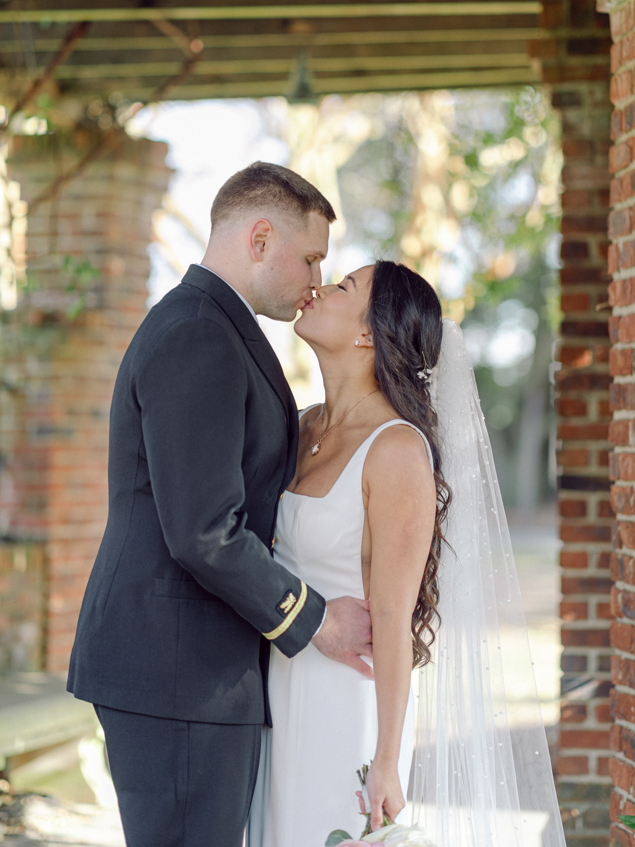 Close up image of a bride and groom standing under a pergola and kissing,  taken by Virginia Beach wedding photographers Glenn and Nadya at the Hermitage Museum and Gardens  