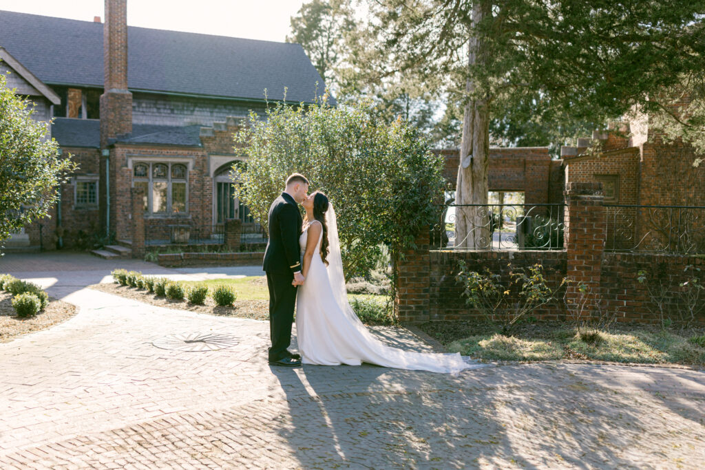 Hermitage Museum and Gardens  wedding photography of a bride and groom standing in front of a historical building next to a fountain , holding hands and kissing, taken by Virginia Beach wedding photographers Glenn and Nadya