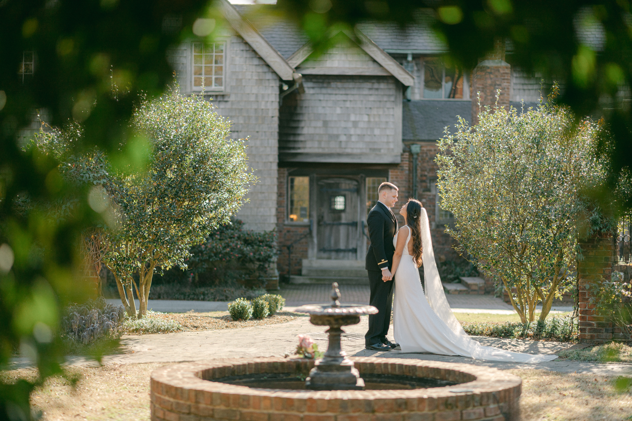 Hermitage Museum and Gardens  wedding photography of a bride and groom standing in front of a historical building next to a fountain , holding hands and looking at each other, taken by Virginia Beach wedding photographers Glenn and Nadya