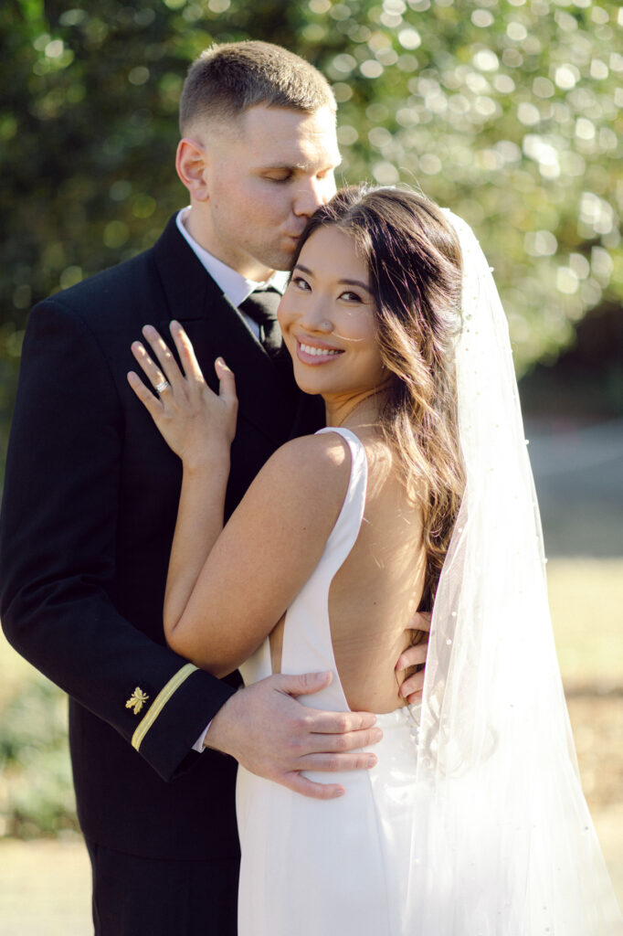 Close up image of a bride and groom hugging each other at the Hermitage Museum and Gardens. The bride is looking back and smiling