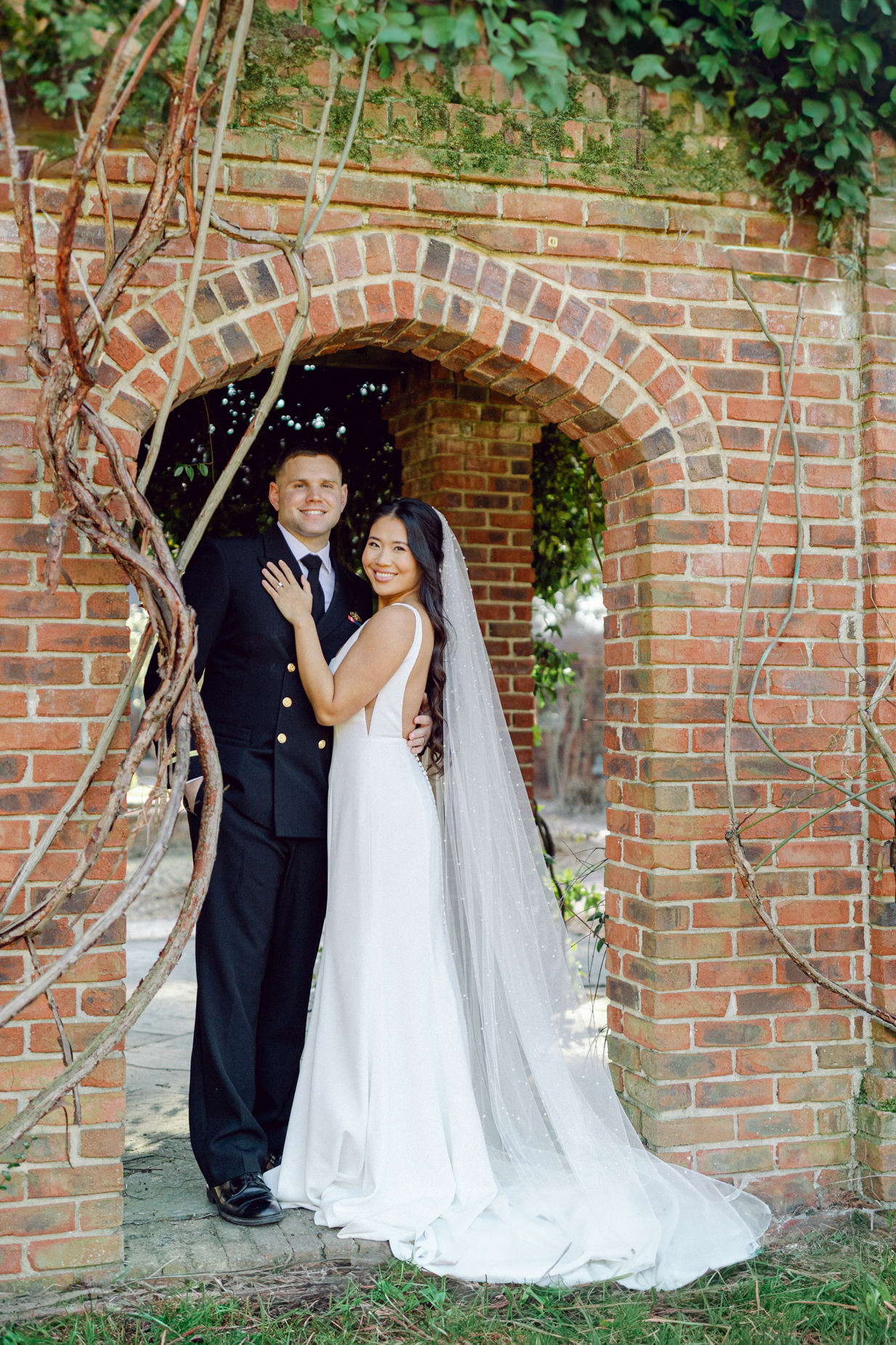 Hermitage Museum and Gardens  wedding photography of a bride and groom standing under a brick arch covered with vines, hugging each other