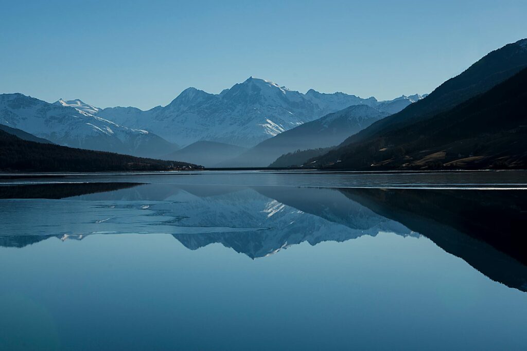 Mountain lake reflecting snow-capped peaks under blue sky